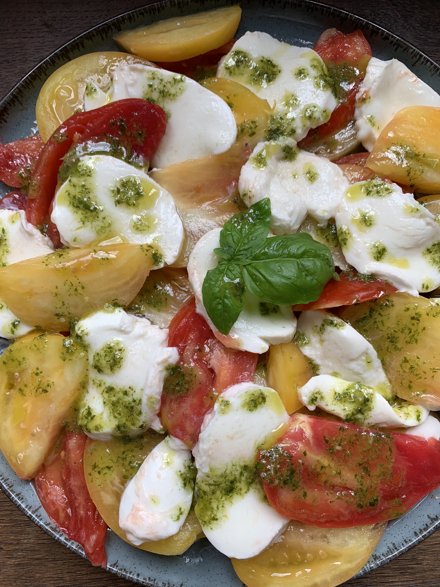 tomato and mozzarella salad with basil oil on a blue plate and basil sprig to decorate
