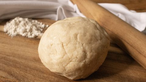 Ball of sourdough discard pastry crust on a board with some flour and a rolling pin