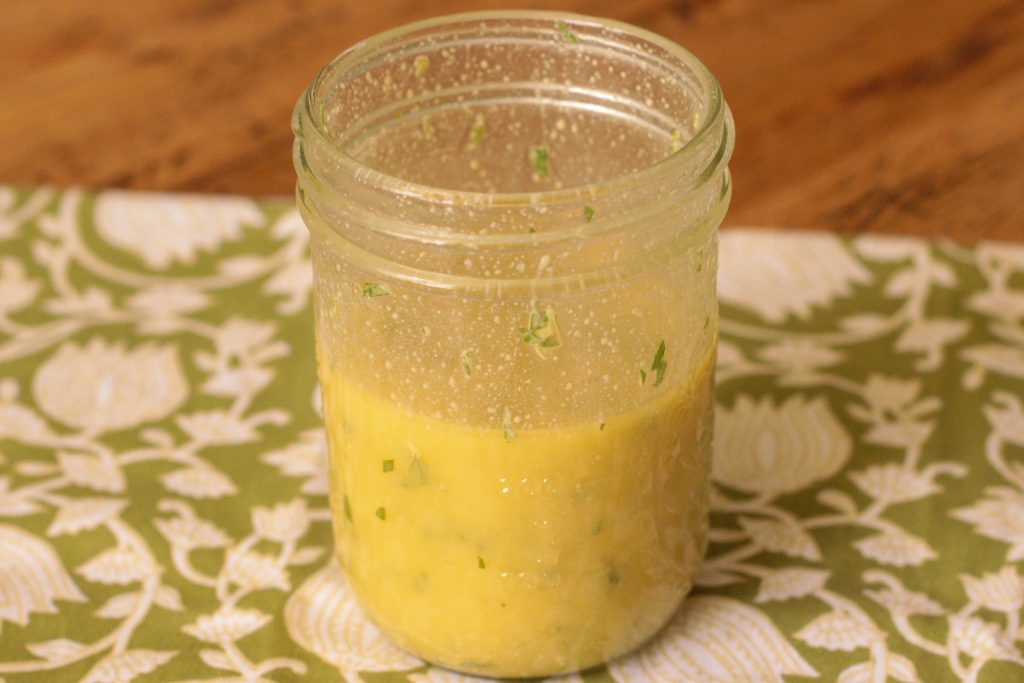 Small jar of quinoa salad dressing with olive oil, apple cider vinegar, mustard, and chopped herbs