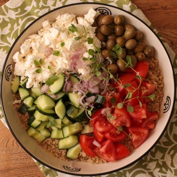 Bowl of quinoa salad with diced cucumber, cherry tomatoes, feta cheese, olives, and fresh herbs