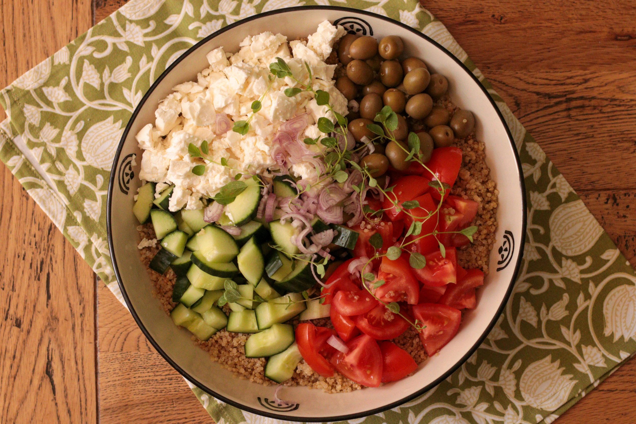 Bowl of quinoa salad with diced cucumber, cherry tomatoes, feta cheese, olives, and fresh herbs