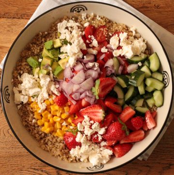 overhead of quinoa salad recipe with strawberries, fresh veggies and feta before tossing