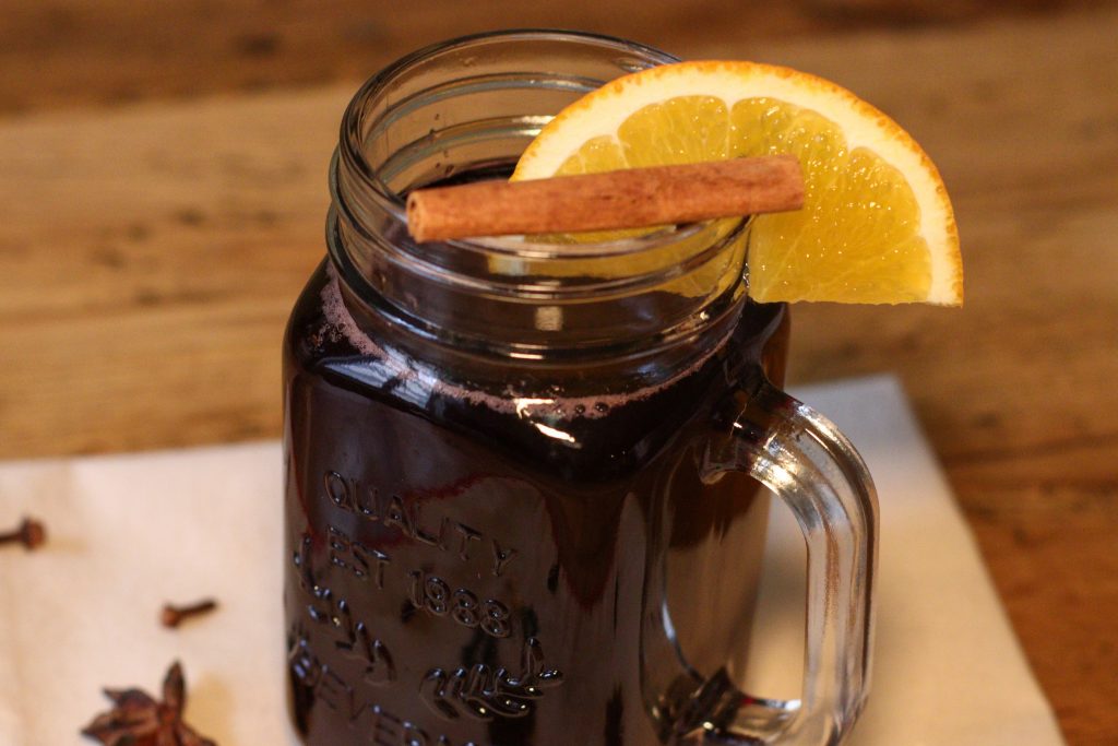 Vin chaud non alcoolisé dans un bocal à anse garni d'une tranche d'orange et d'un bâton de cannelle.