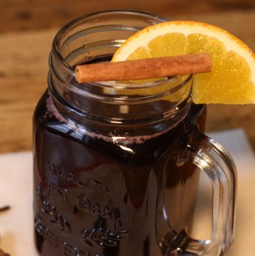 Vin chaud non alcoolisé dans un bocal à anse garni d'une tranche d'orange et d'un bâton de cannelle.