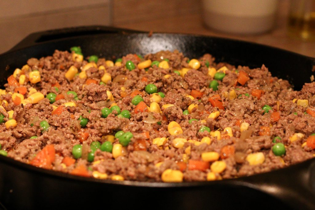 sauce à la viande avec pois et maïs dans une poêle en fonte