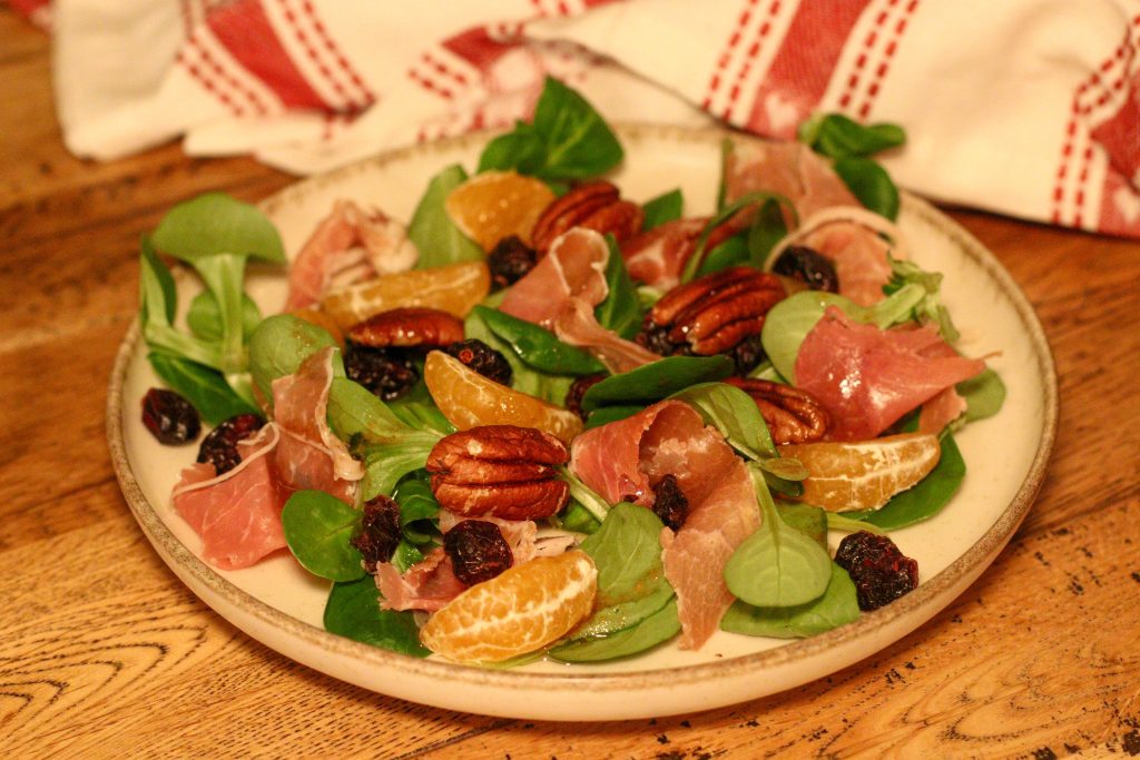Salade de Noël avec clémentines, noix de pécan et proscuitto sur une petite assiette avec un torchon de Noël