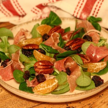 Salade de Noël avec clémentines, noix de pécan et proscuitto sur une petite assiette avec un torchon de Noël