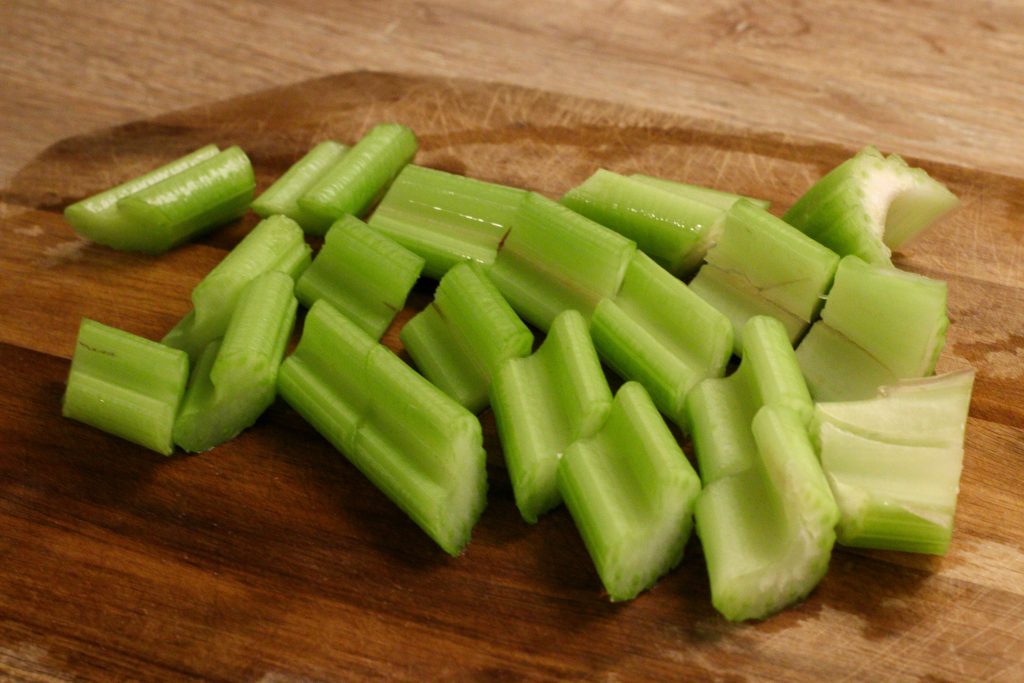 céleri coupé en morceaux de 1 pouce sur une planche à découper