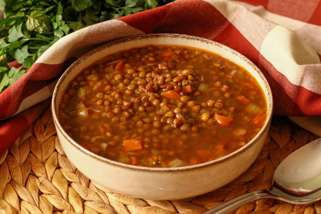 Soupe de lentilles au lard dans un bol crème et torchon à carreaux bordeaux et crème