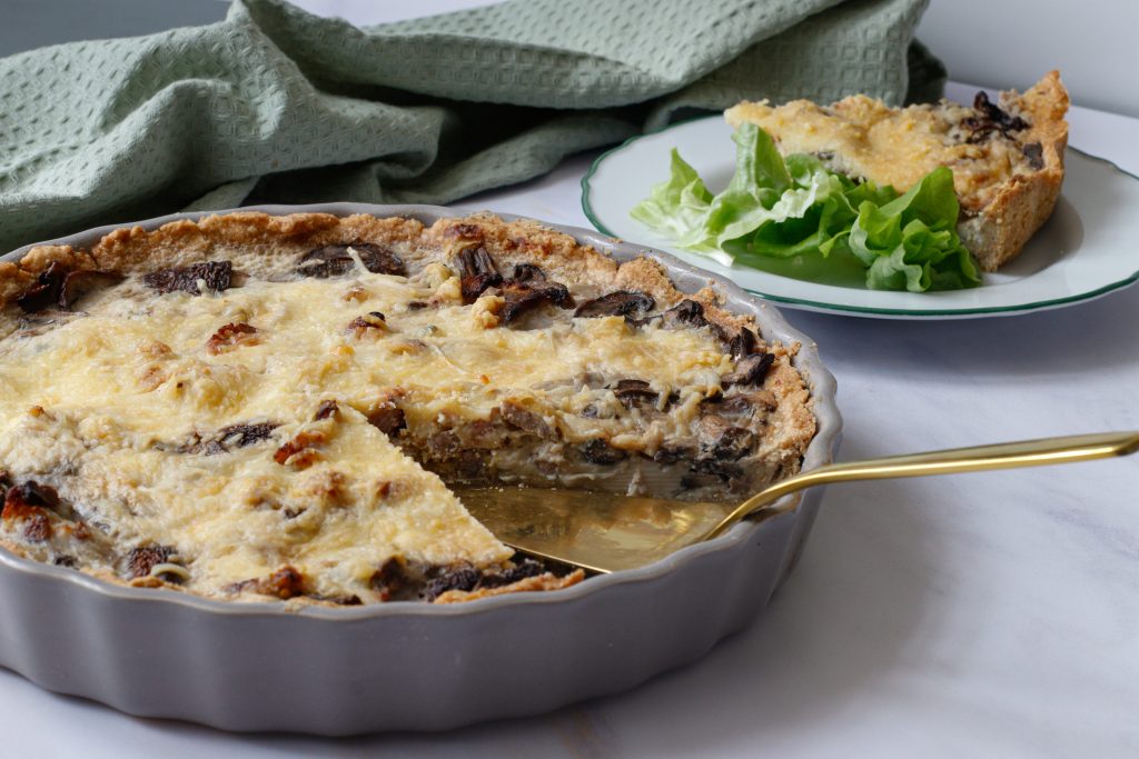 Quiche aux champignons et au bacon avec une tranche entière découpée. Tranche de quiche sur une assiette au fond d'une salade verte
