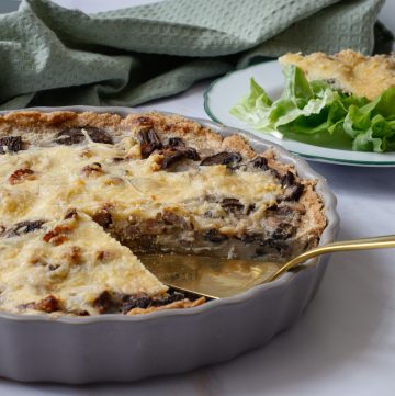 Quiche aux champignons et au bacon avec une tranche entière découpée. Tranche de quiche sur une assiette au fond d'une salade verte