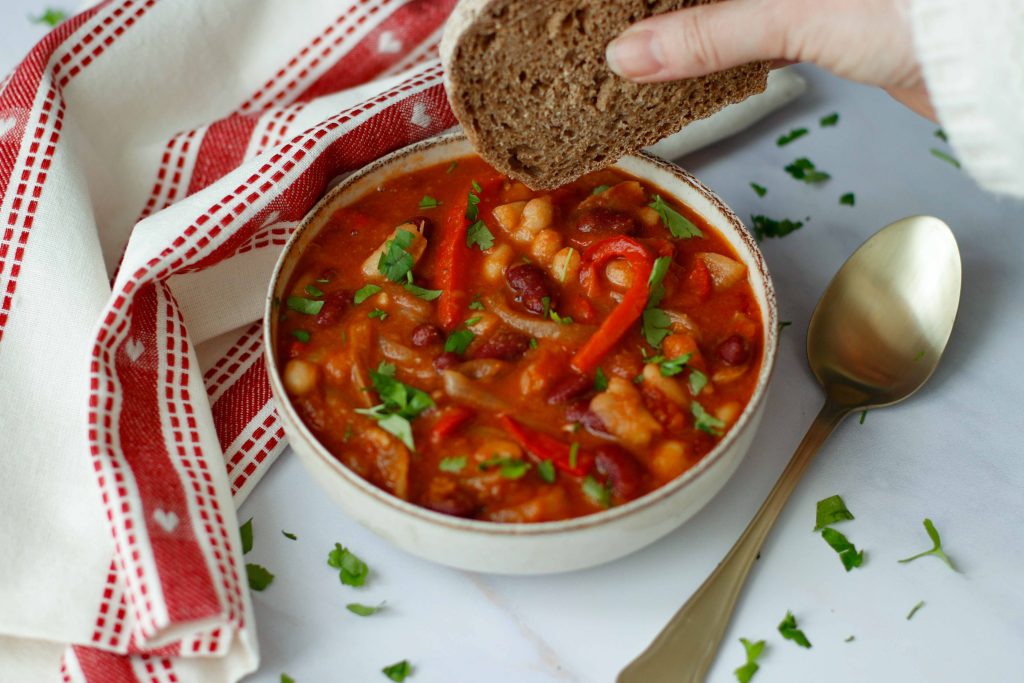 hand dipping wholegrain bread into bowl of simple bean stew