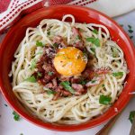 creamy pastat carbonara shown in a red bowl with lardons and an egg yolk on top