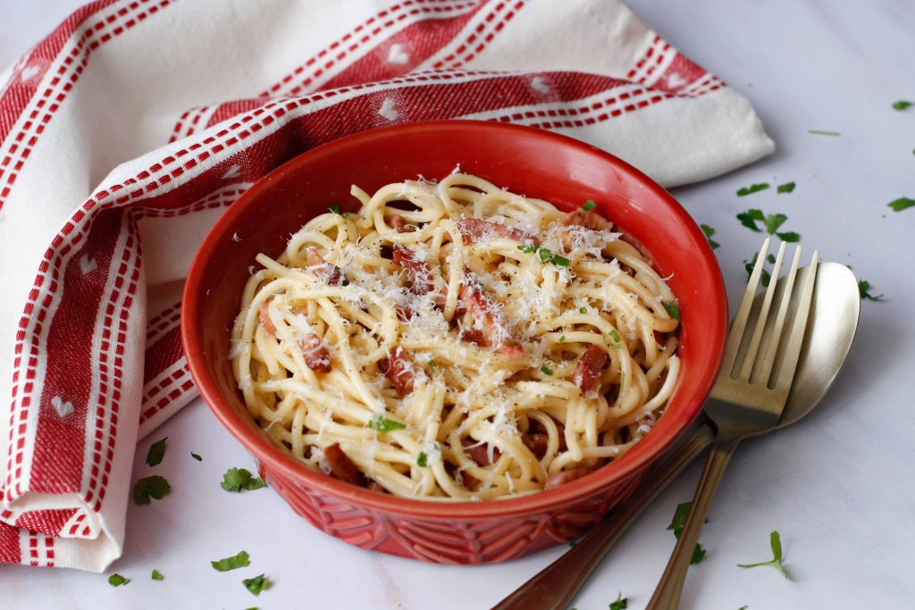 Carbonara sauce recipe served with spaghetti in a red bowl with a fork and spoon on the side