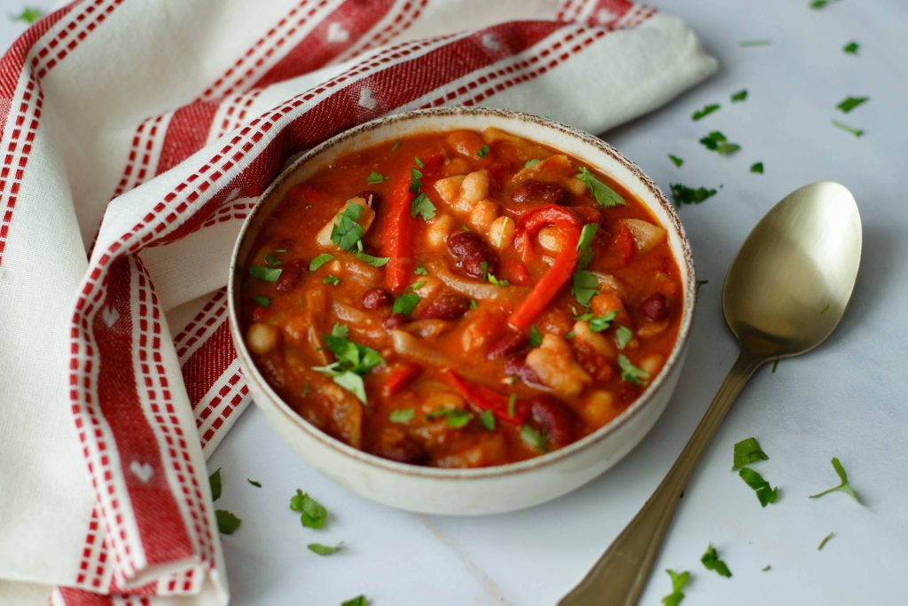 hearty bean stew in a bowl with golden spoon and red and white tea towel