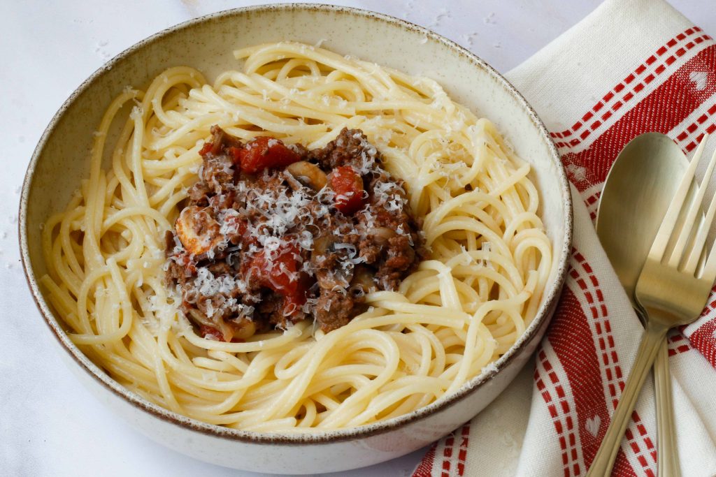 recette de spaghetti bolognaise servie dans un petit bol avec une nappe rouge et blanche et des couverts dorés