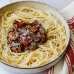 recette de spaghetti bolognaise servie dans un petit bol avec une nappe rouge et blanche et des couverts dorés