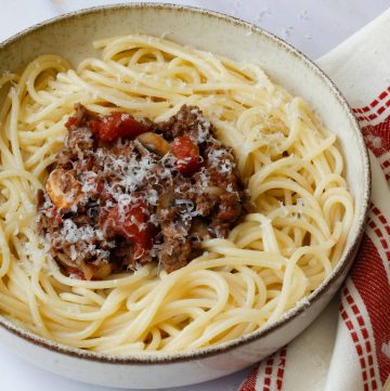 recette de spaghetti bolognaise servie dans un petit bol avec une nappe rouge et blanche et des couverts dorés