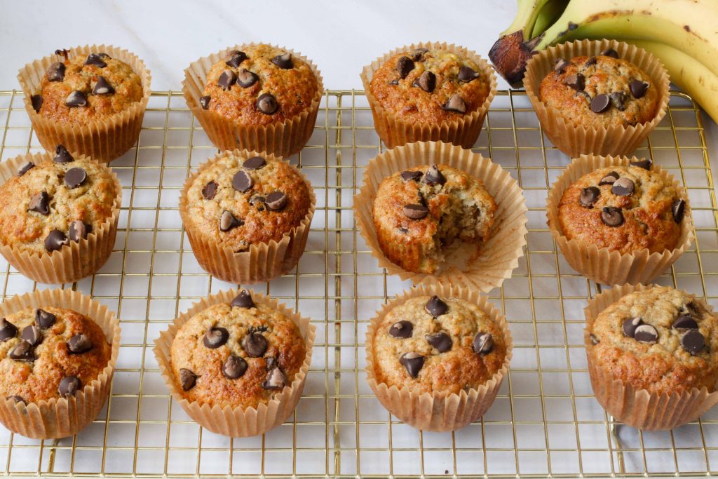Overhead flat lay of sourdough oatmeal muffins in paper liners with extra chocolate chips. one muffin has a bite taken out of it