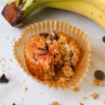 close up of Sourdough Banana Oat Muffins with Chocolate Chips bitten into with bananas and choco chips in background